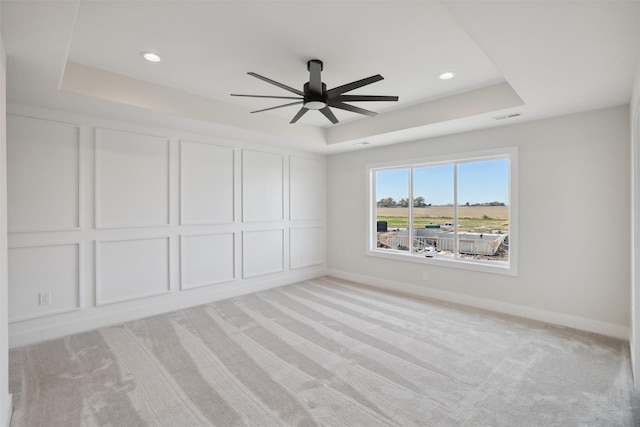 unfurnished bedroom featuring a raised ceiling, light carpet, a decorative wall, and baseboards