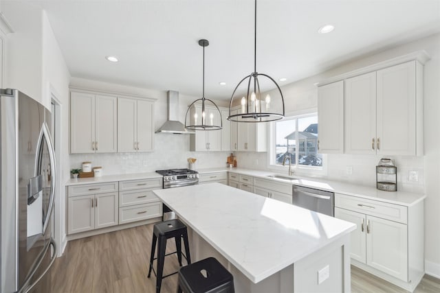 kitchen featuring stainless steel appliances, a sink, white cabinets, a center island, and wall chimney exhaust hood