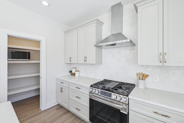 kitchen featuring white cabinets, light stone countertops, stainless steel gas range, wall chimney range hood, and backsplash