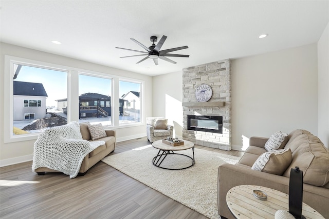 living area with recessed lighting, a stone fireplace, baseboards, and wood finished floors