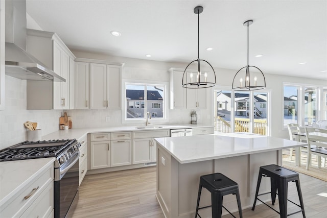 kitchen featuring stainless steel appliances, hanging light fixtures, white cabinetry, a sink, and wall chimney exhaust hood