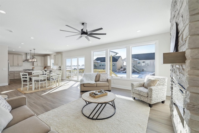 living area with recessed lighting, light wood-style floors, a ceiling fan, a stone fireplace, and baseboards