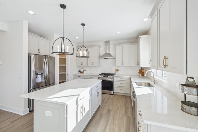 kitchen featuring stainless steel appliances, white cabinetry, a sink, a kitchen island, and wall chimney exhaust hood