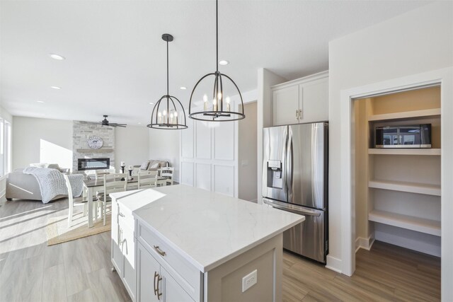 kitchen with a center island, decorative light fixtures, a fireplace, stainless steel refrigerator with ice dispenser, and white cabinets