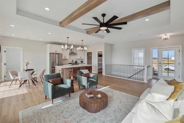 living room featuring sink, a raised ceiling, light hardwood / wood-style flooring, beamed ceiling, and ceiling fan with notable chandelier