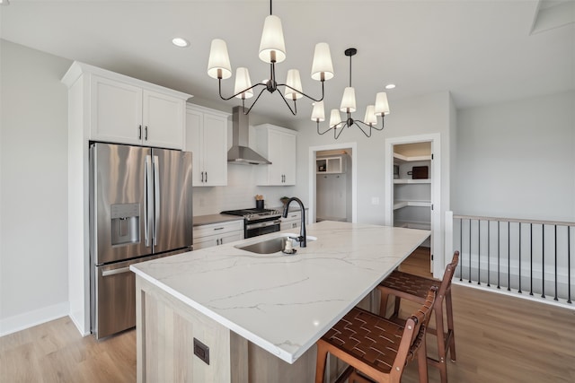 kitchen with white cabinets, wall chimney exhaust hood, a kitchen island with sink, and appliances with stainless steel finishes