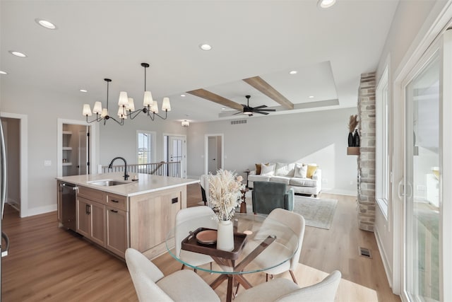 kitchen with stainless steel dishwasher, sink, decorative light fixtures, light hardwood / wood-style flooring, and an island with sink