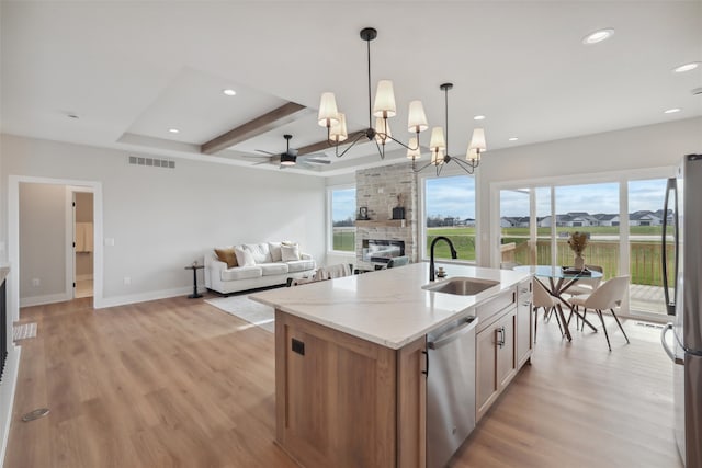 kitchen featuring light stone countertops, stainless steel appliances, sink, decorative light fixtures, and an island with sink