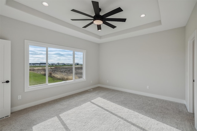 carpeted spare room featuring ceiling fan and a raised ceiling