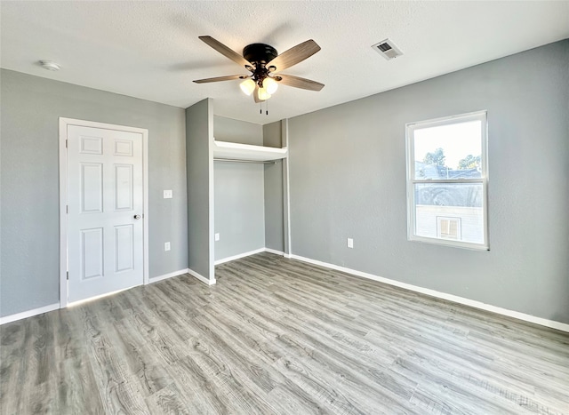 unfurnished bedroom featuring a closet, a textured ceiling, light hardwood / wood-style floors, and ceiling fan