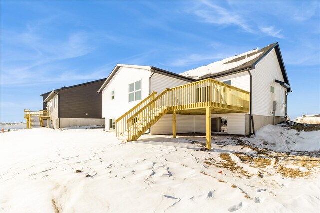 snow covered house featuring stairs and a deck