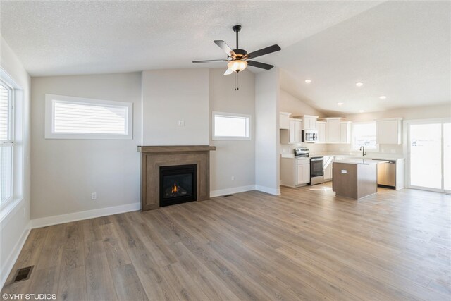 unfurnished living room with a healthy amount of sunlight, light wood-style floors, visible vents, and vaulted ceiling