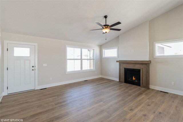 unfurnished living room with vaulted ceiling, a lit fireplace, baseboards, and wood finished floors