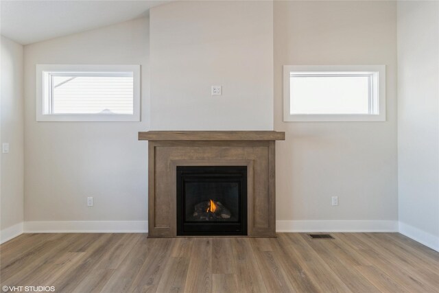 unfurnished living room with lofted ceiling, a warm lit fireplace, visible vents, and wood finished floors