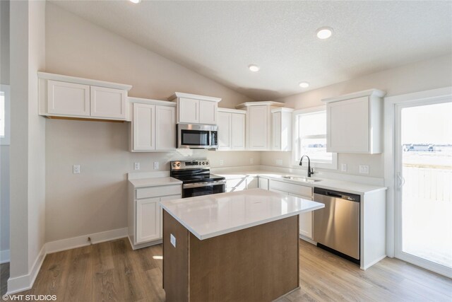 kitchen featuring a kitchen island, appliances with stainless steel finishes, light countertops, white cabinetry, and a sink