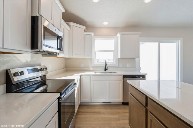 kitchen with appliances with stainless steel finishes, white cabinetry, a sink, and light stone countertops