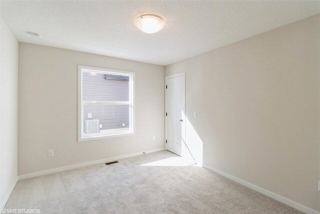 empty room with light carpet, a textured ceiling, visible vents, and baseboards