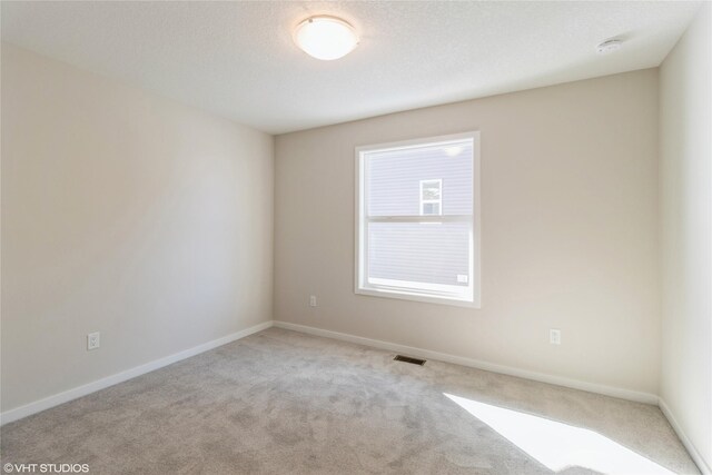 unfurnished room with light carpet, a textured ceiling, visible vents, and baseboards