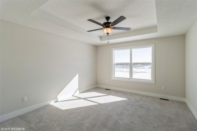 empty room with a raised ceiling, light colored carpet, visible vents, a textured ceiling, and baseboards