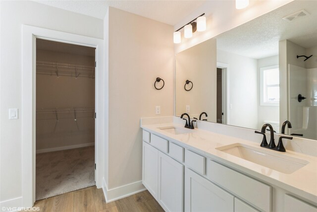 full bath featuring a spacious closet, wood finished floors, a sink, and visible vents