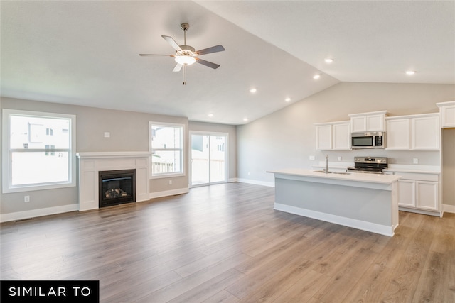 kitchen with stainless steel appliances, vaulted ceiling, light wood-type flooring, and white cabinets