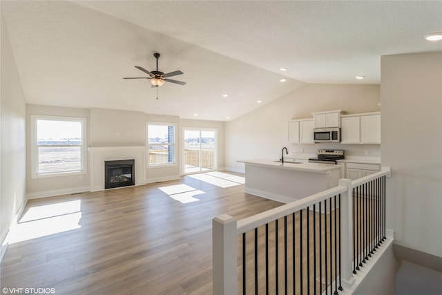 unfurnished living room with lofted ceiling, sink, light hardwood / wood-style flooring, ceiling fan, and a textured ceiling