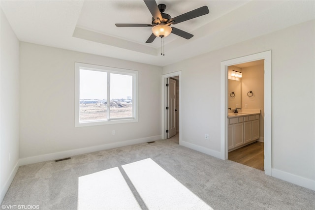 unfurnished bedroom featuring connected bathroom, a tray ceiling, and light colored carpet