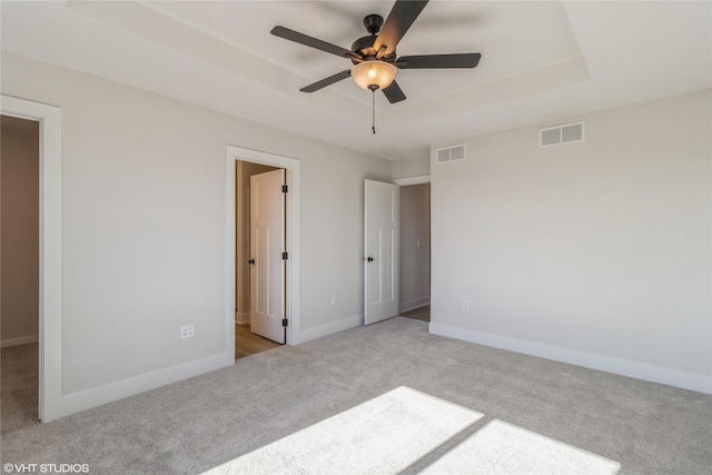 unfurnished bedroom with ensuite bathroom, light colored carpet, and a tray ceiling