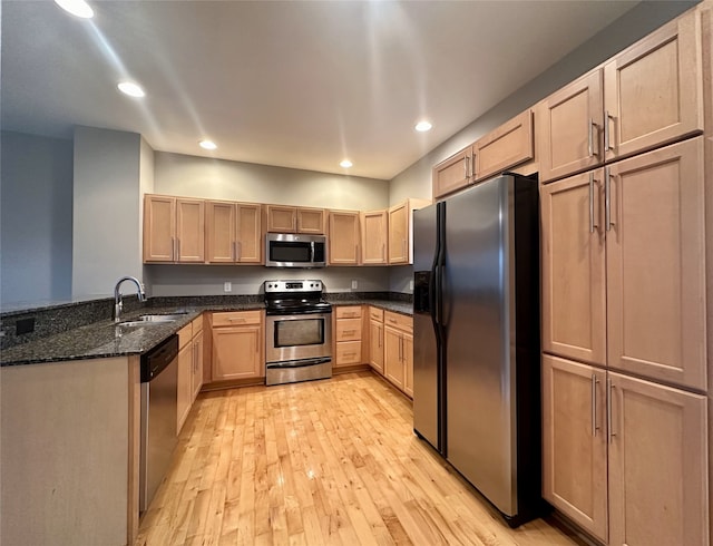 kitchen with light hardwood / wood-style floors, dark stone countertops, stainless steel appliances, and sink