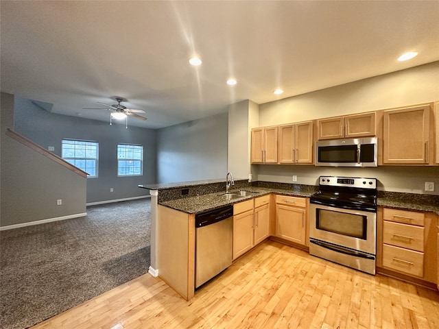 kitchen with appliances with stainless steel finishes, sink, kitchen peninsula, dark stone countertops, and light hardwood / wood-style flooring