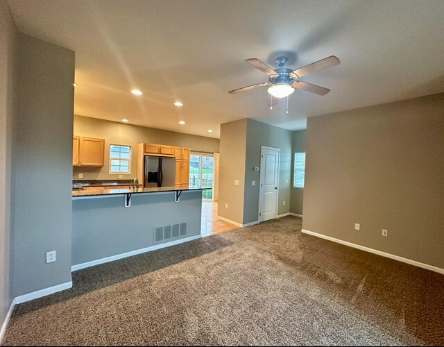 kitchen with a breakfast bar area, stainless steel fridge, light brown cabinets, and dark colored carpet