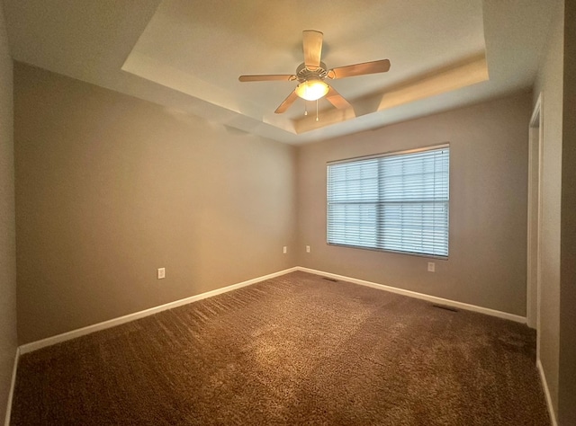 carpeted spare room with ceiling fan and a tray ceiling