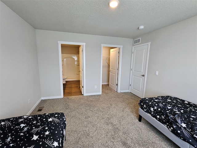 carpeted bedroom with a spacious closet, connected bathroom, a textured ceiling, and a closet