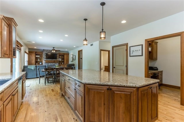 kitchen featuring a kitchen island, a stone fireplace, decorative light fixtures, light wood-type flooring, and light stone counters