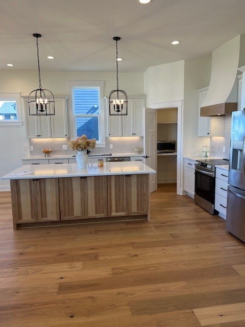 kitchen featuring stainless steel appliances, white cabinets, a spacious island, and light wood-type flooring