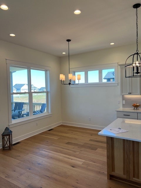 unfurnished dining area with a chandelier, a healthy amount of sunlight, and wood-type flooring