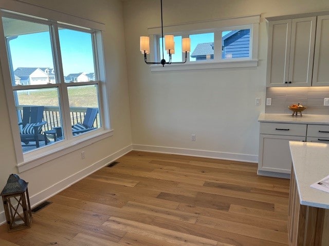 unfurnished dining area featuring light hardwood / wood-style floors, a healthy amount of sunlight, and a chandelier