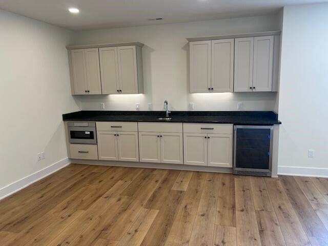 kitchen with beverage cooler, white cabinets, sink, and light hardwood / wood-style flooring