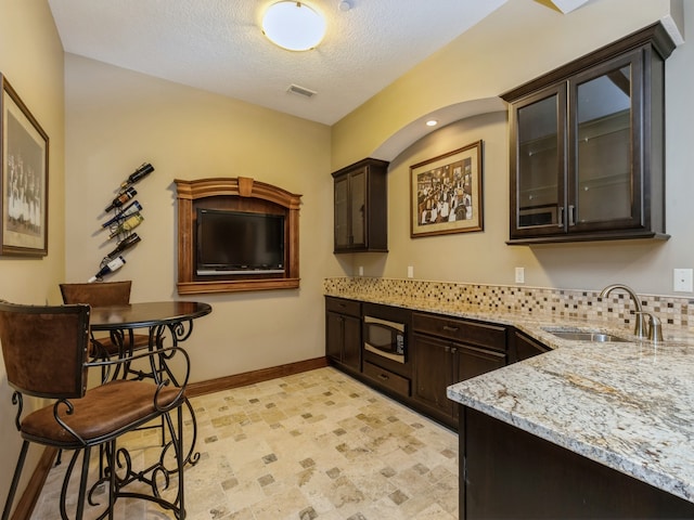 kitchen with light stone counters, visible vents, a sink, built in microwave, and baseboards