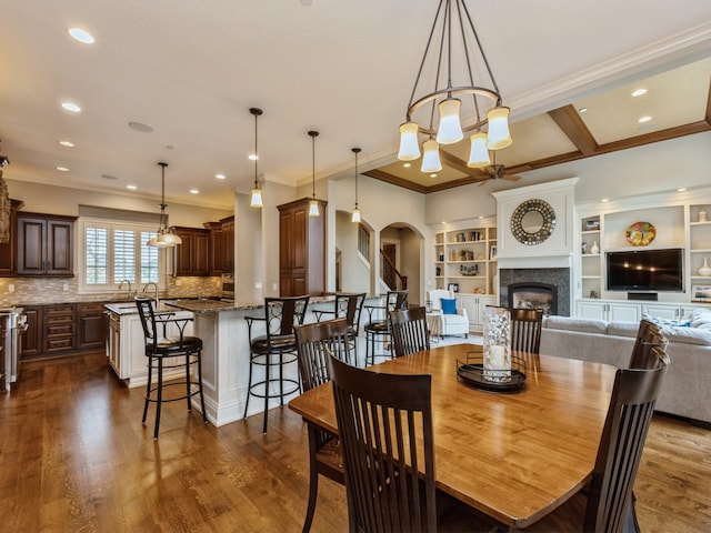 dining area featuring arched walkways, a glass covered fireplace, dark wood-style flooring, a chandelier, and recessed lighting