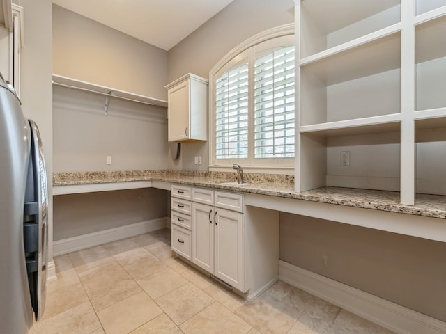 interior space with light stone counters, built in desk, open shelves, freestanding refrigerator, and a sink