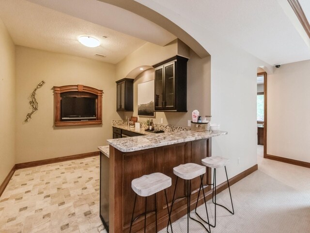 3123 162nd St, Urbandale, IA 50323 - kitchen featuring arched walkways, a breakfast bar area, baseboards, and light stone counters