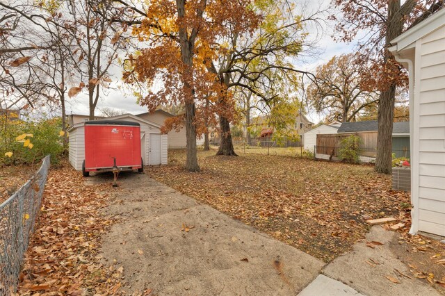 view of yard featuring an outdoor structure, fence, a storage shed, and concrete driveway