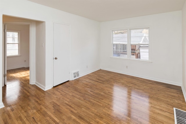 empty room with wood finished floors, a wealth of natural light, and visible vents