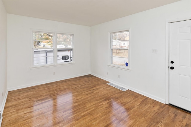 empty room featuring wood finished floors, baseboards, and visible vents