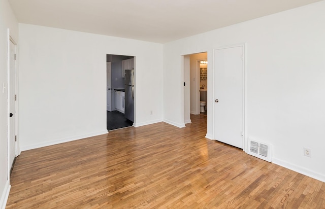 unfurnished bedroom featuring visible vents, baseboards, connected bathroom, wood finished floors, and freestanding refrigerator