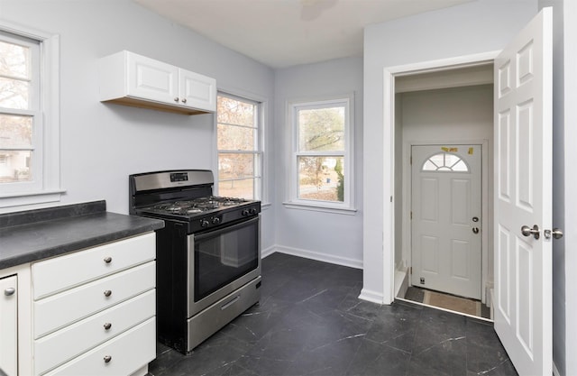 kitchen featuring white cabinets, dark countertops, gas range, and baseboards