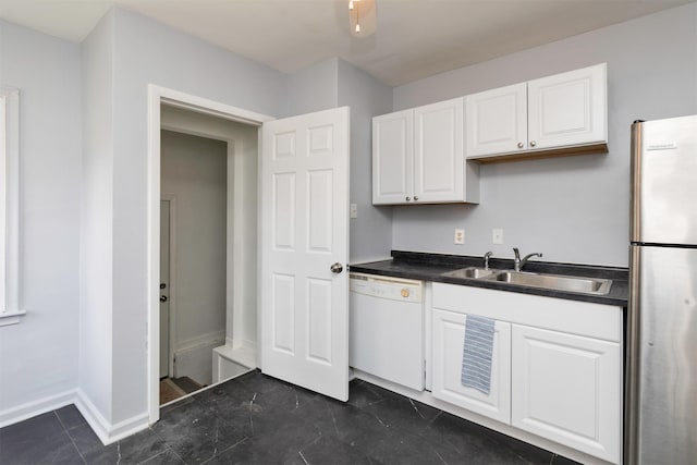 kitchen featuring a sink, freestanding refrigerator, white dishwasher, dark countertops, and white cabinets