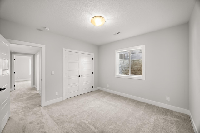 unfurnished bedroom featuring a textured ceiling, light colored carpet, and a closet