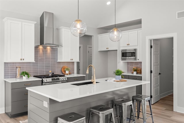 kitchen featuring a kitchen island with sink, white cabinetry, stainless steel appliances, and wall chimney range hood